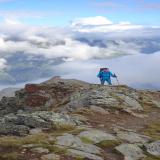 Une randonneuse marche sur une ligne de crête et laisse derrière elle un refuge de montagne dans les nuages