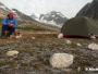 Un trekkeur solitaire mange à côté de sa tente au Groenland Est. Il est protégé par un fusil.