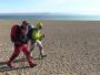 Deux randonneurs progressent dans une zone aride le long d'un immense lac salé.