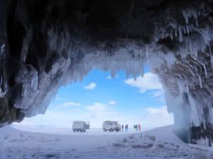 Des véhicule sont arrêtés sur la glace du Lac Baïkal, à côté de grottes où pendent des stalactites