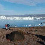 Deux randonneurs se tiennent dans un campement juste au bord du fjord Sermilik plein d'icebergs.